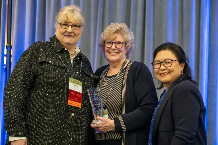 Three nurse leaders posing together, the one in the center holding an award