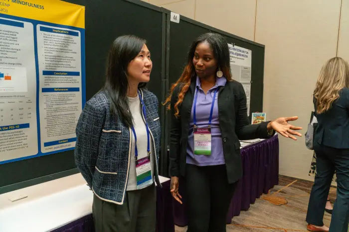 Two attendees at a research poster, one gesturing as she explains it