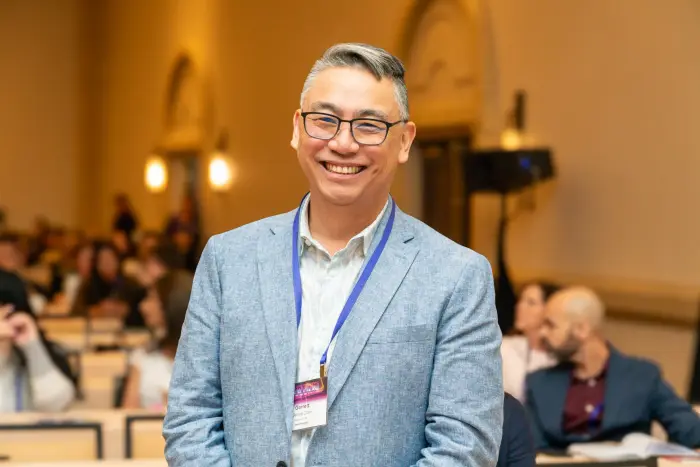 A candid portrait of a smiling attendee in a light blazer, audience behind