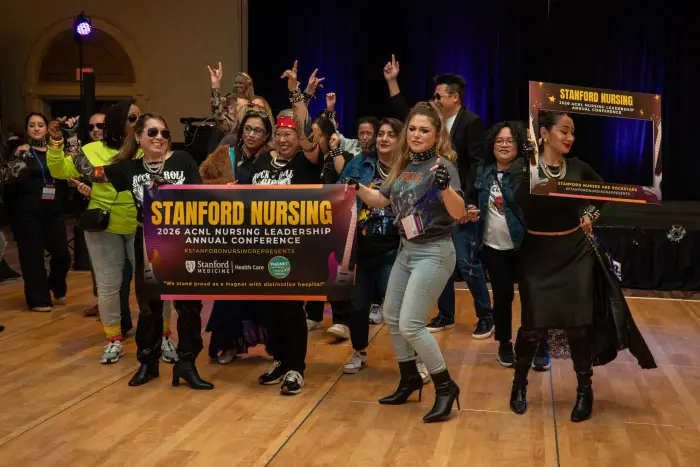 A large group cheering under a Stanford Nursing conference backdrop
