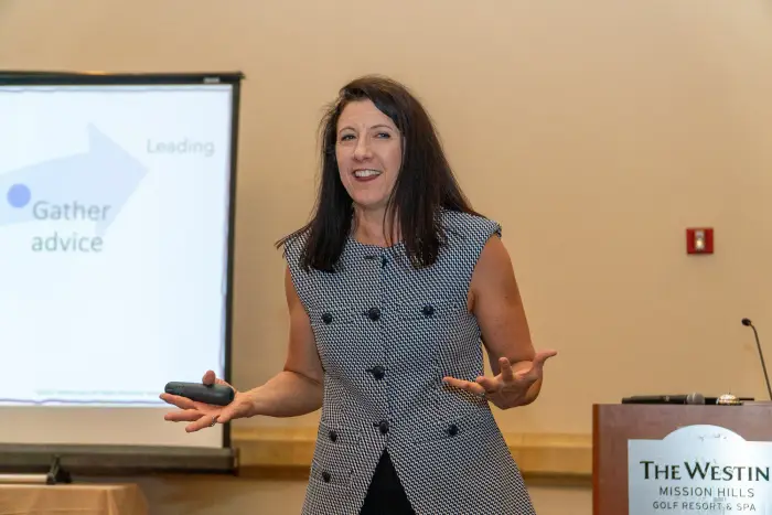 A speaker presenting beside a podium with a slide projected behind her