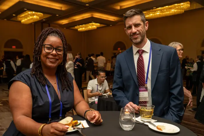 Two attendees with plates and drinks smiling together at a reception