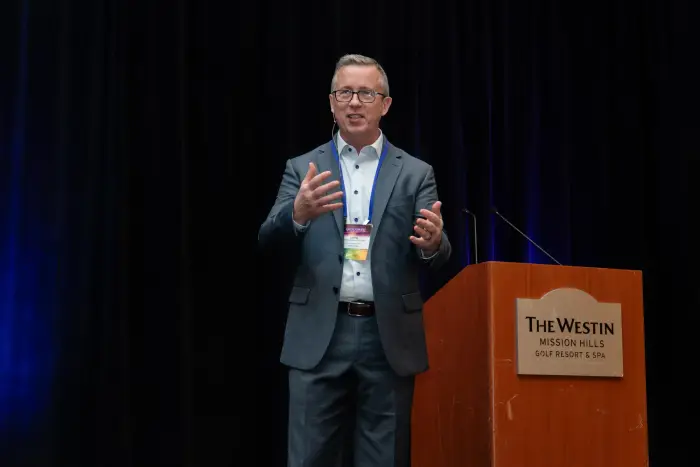 A keynote speaker addressing the room from a podium under stage lighting